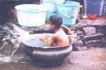 Un enfant se baigne et joue dans une bassine, dans la rue